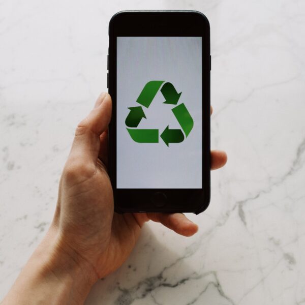 From above view of faceless person holding mobile phone with white screen and green recycle logo above marble surface